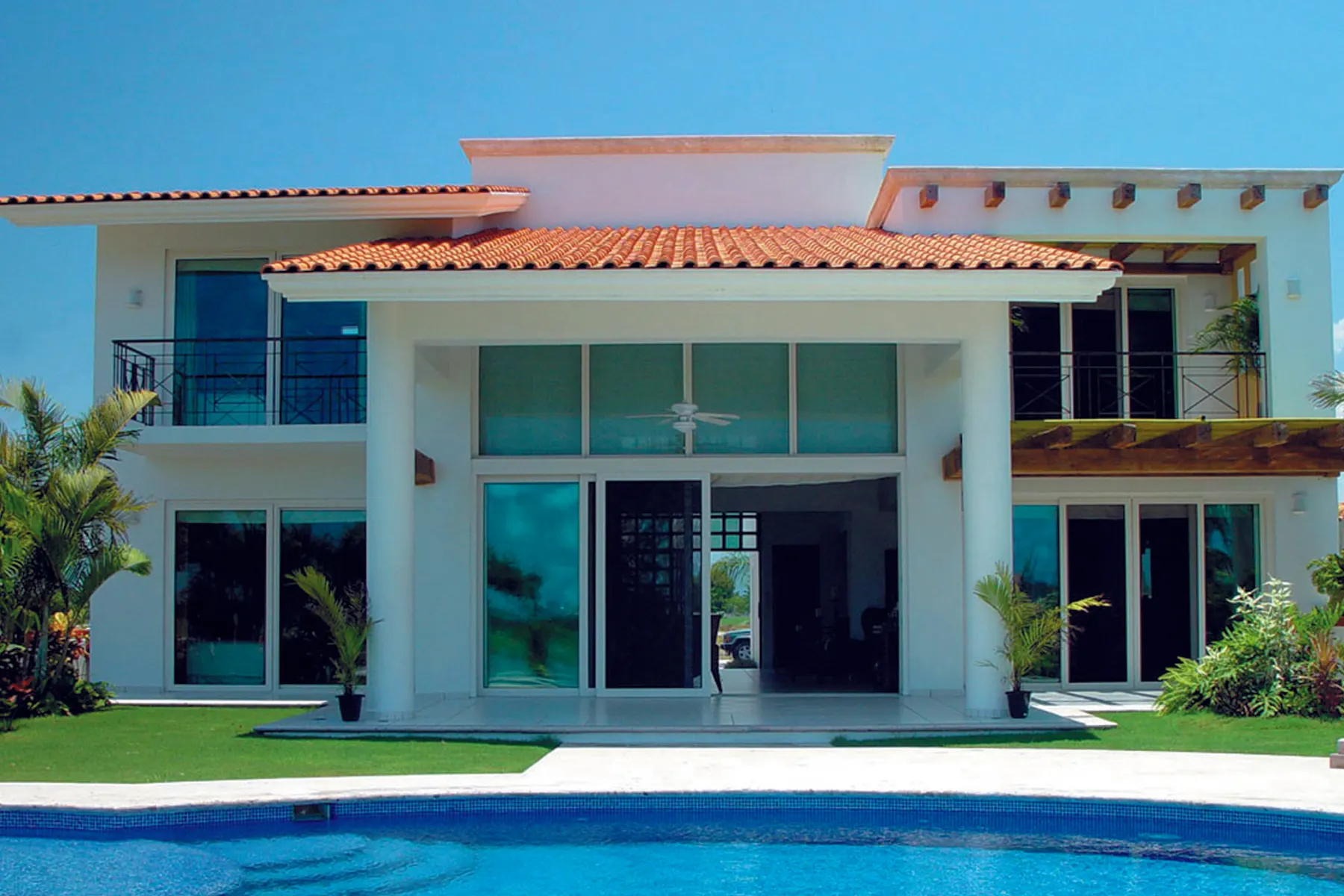 Fachada de una vivienda unifamiliar con grandes paños de vidrio en la planta baja abiertos a la piscina. En unifamiliar, la salida al jardín es el hueco donde la elevable más se justifica.